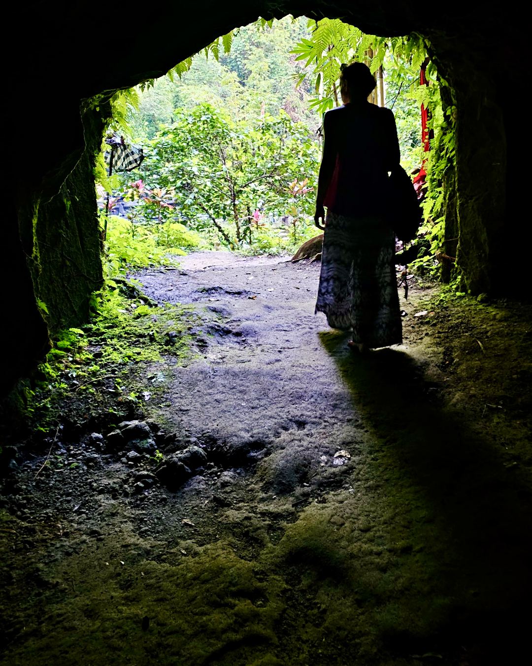 Eine Frau steht am Ausgang eines Steintunnels und blickt in grünen Wald.