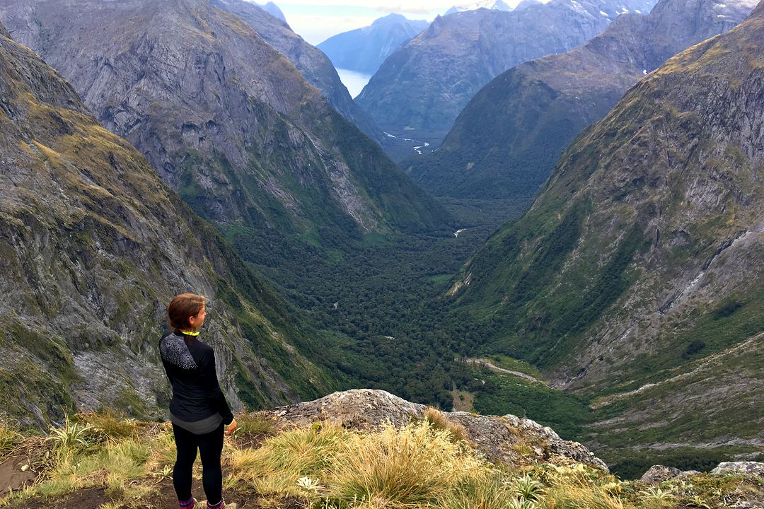 A woman standing on a ridge above a deep glacial valley.