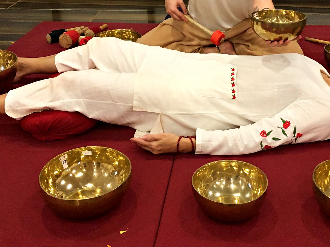 A practitioner holding a singing bowl beside a person lying on a mat, brass bowls placed around them.